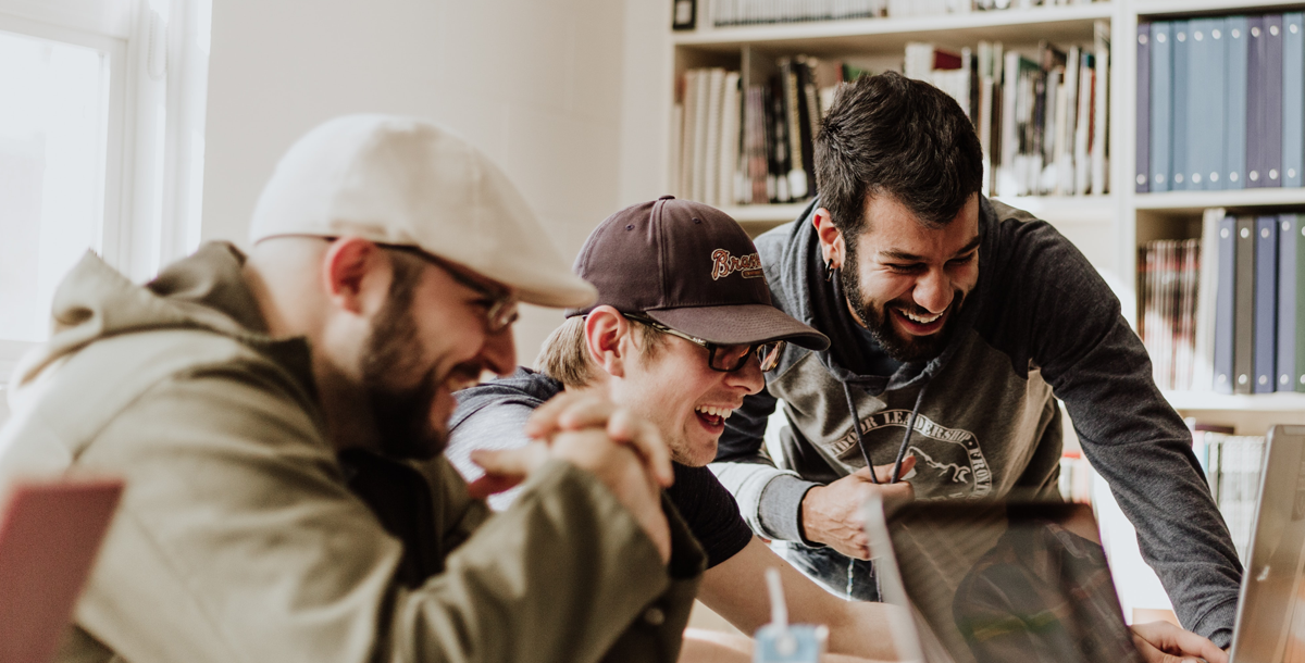 Photo by Priscilla Du Preez on Unsplash - group of excited students wearing baseball hats around a computer.